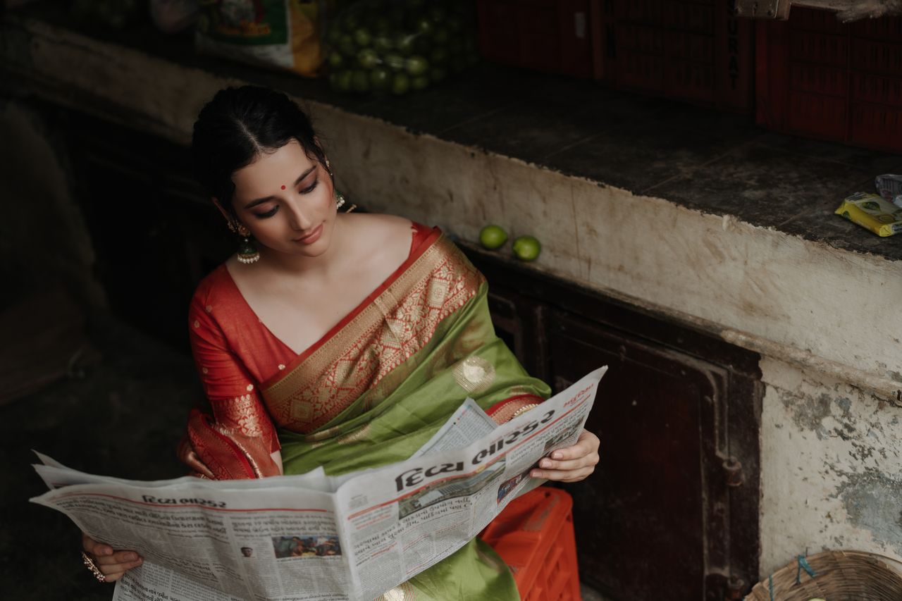 Elegant woman in a saree engrossed in reading a newspaper indoors with ambient lighting.